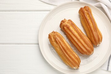Fresh tasty eclairs on white wooden table, top view. Space for text