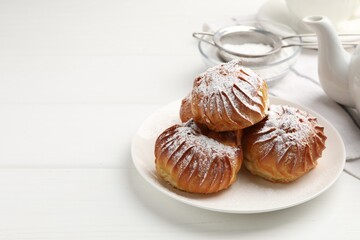 Tasty profiteroles with powdered sugar served on white wooden table. Space for text
