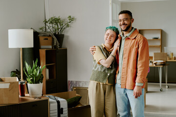 Young adult Caucasian woman with short green hair and young adult man standing together smiling and hugging in modern apartment 
