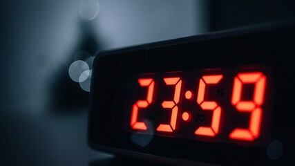 Digital alarm clock displaying 23:59 in red LED numbers against a dark blurry background