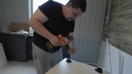 Professional furniture assembler working indoors, using a cordless electric drill to screw parts together while putting up a new kitchen cabinet during a home improvement and renovation project.