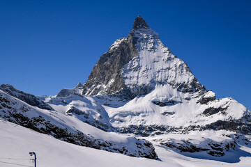 Close view of the Matterhorn covered in winter snow, rising sharply under a deep blue sky. Iconic Swiss alpine landscape with dramatic textures and prisitine mountain scenery.