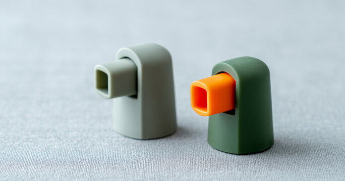 A pair of inhalers with a green and orange color scheme on display against grey fabric background