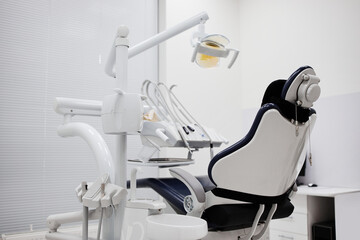 Empty dental chair standing in modern dental office with professional equipment arranged around treatment area, clinical setting prepared for patient appointment, no people visible