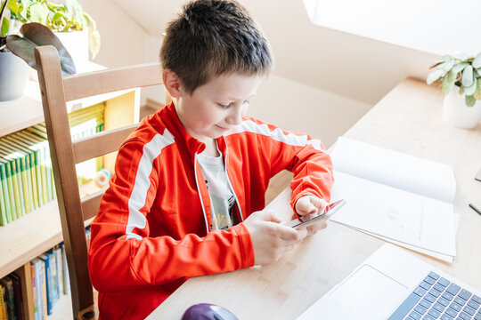 Boy using smartphone, distracted from school homework studying