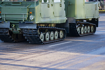 Fototapeta premium Tracked military transport vehicles with connected chassis and visible suspension components moving along an urban roadway during defense mobility readiness