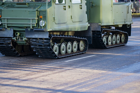 Tracked military transport vehicles with connected chassis and visible suspension components moving along an urban roadway during defense mobility readiness