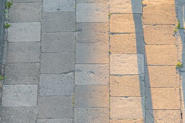 Bright sun illuminates textured stone pavement in a modern city, casting long shadows Diagonal perspective adds depth to the tranquil, people-less scene