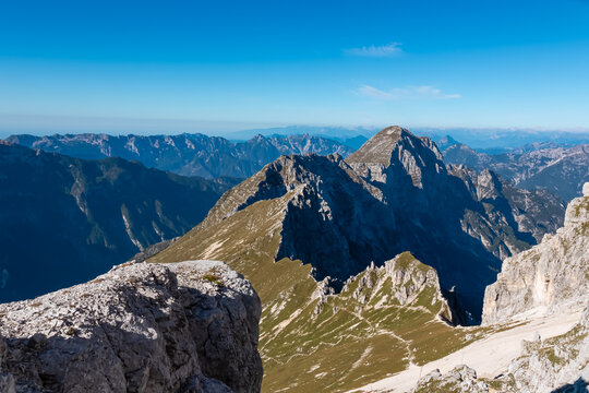 A high mountain ridge covered in grass and rock leads towards the summit of Jof di Montasio. The panoramic landscape of the Julian Alps showcases deep valleys and peaks in Friuli Venezia Giulia.