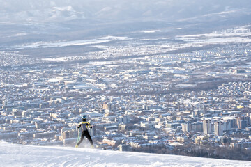 Skier on snowy mountain overlooking city in winter haze
