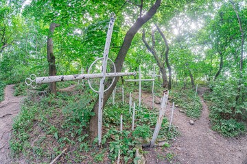 Wooden cross with rosary bead detail, surrounded by scattered wooden markers in a forested setting...