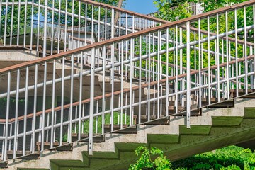 Concrete staircase with decorative metal railings, leading to a bridge in a modern city scene The railings are alternating green and blue, emphasizing the number of steps under bright daylight
