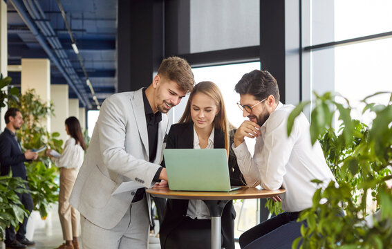 Smiling friendly helpful colleagues working, young diverse businesspeople at desk brainstorm, discuss business ideas together at briefing, cooperate working on laptop at meeting in office, teamwork