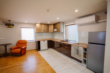 Modern kitchen interior featuring sleek cabinetry, wooden flooring, and a cozy armchair, illuminated by natural light from large windows, creating a warm and inviting atmosphere
