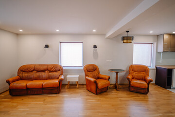 Cozy living room featuring two brown leather sofas and an armchair, illuminated by soft lighting, with wooden flooring and a small table, creating a warm and inviting atmosphere
