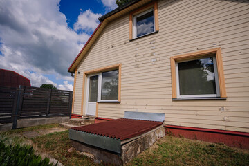 Residential house exterior featuring wooden siding, large windows, and a small porch area, surrounded by green grass and a wooden fence, showcasing a peaceful suburban environment