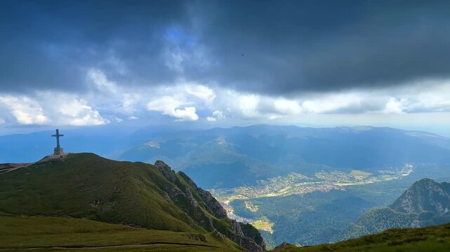 Dark dramatic cloudscape covers the sky over the Southern Carpathians. View on the Cross Memorial on the green Caraiman Peak in Bucegi Mountains, Romania.