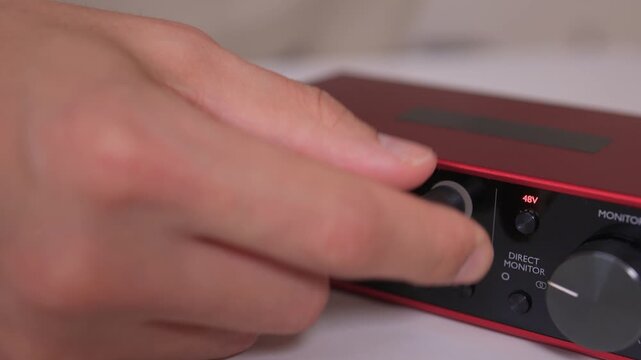 Adjusting external sound card knob, Precise control over audio output through knob rotation, Modifying sound levels using detailed textured dial on external audio interface