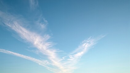 A blue sky with wispy white clouds and contrails creating a serene and airy atmosphere above