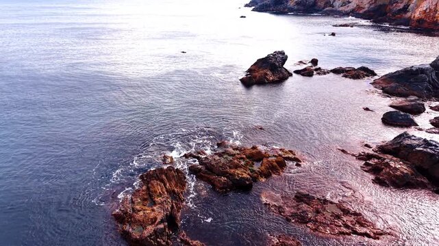 Flying above the rocks sticking out from waterscape. Circling around the stones in the sea near the shore.