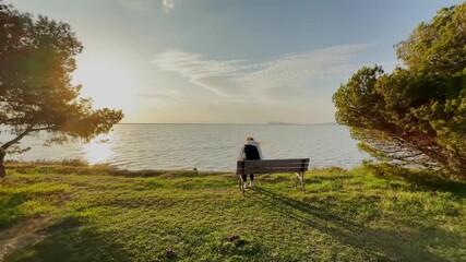 A woman sitting on bench between two trees watching beautiful ocean sunset view at Gediz Delta