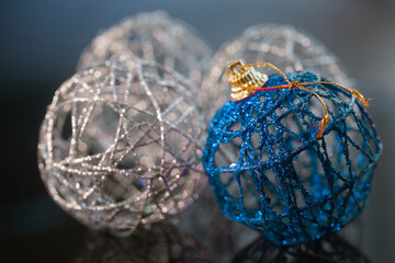 Fototapeta premium Close up of blue and silver woven Christmas balls with glitter on dark reflective background. Handmade thread baubles for winter holiday decoration and greeting card. Photo