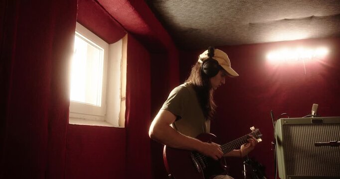 Guitarist wearing headphones playing electric guitar in a soundproof recording studio