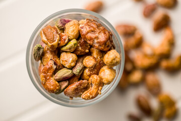 Nuts coated in sugar glaze in jar on white table. Top view.