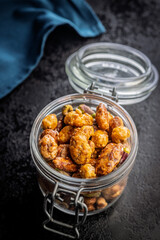 Nuts coated in sugar glaze in jar on black table.