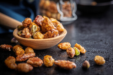 Nuts coated in sugar glaze on wooden spoon on black table.
