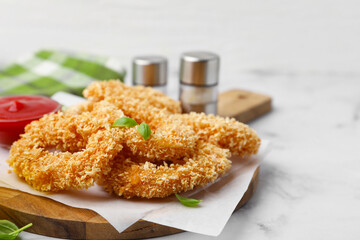 Deep fried squid rings, basil and ketchup on light marble table, closeup. Space for text