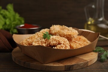 Deep fried squid rings with parsley in takeaway paper box on wooden table, closeup