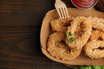 Deep fried squid rings with parsley in takeaway paper box, fork and ketchup on wooden table, flat lay. Space for text