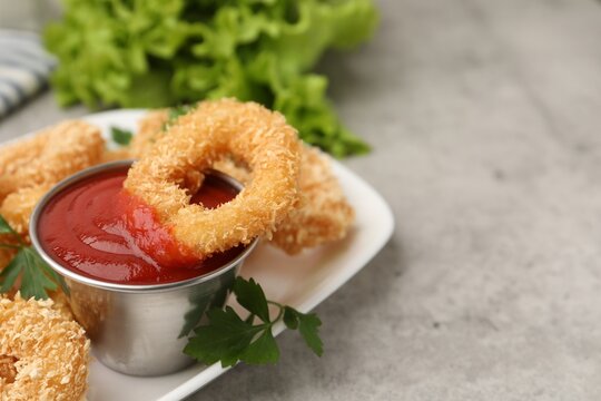 Deep fried squid rings with parsley and ketchup on grey textured table, closeup. Space for text - Powered by Adobe