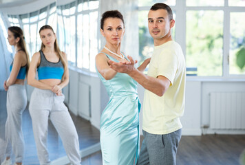 Obraz premium Concentrated slim woman, dance instructor, showcasing elegant waltz moves with male student as female partner attentively watching standing in background against mirror wall in studio