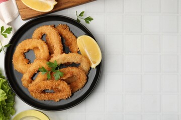 Deep fried squid rings with parsley and lemon slice on white tiled table, flat lay. Space for text