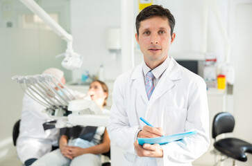 Adult male nurse taking notes while examining patient in dental office