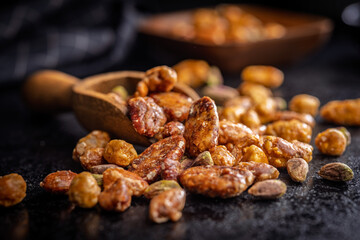Nuts coated in sugar glaze in scoop on black table.