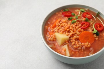 Delicious lentil soup with vegetables in bowl on light grey table, closeup. Space for text