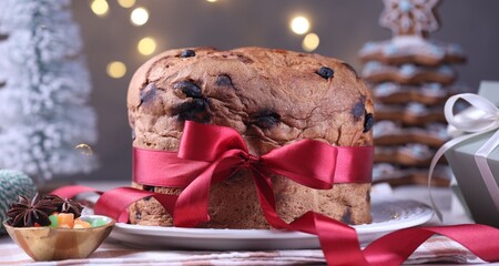 Tasty Christmas panettone cake decorated with red ribbon on table against blurred lights, closeup. Bokeh effect