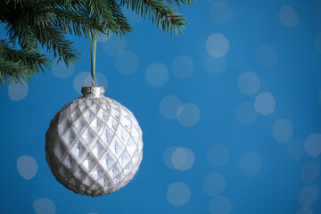 Beautiful ball on Christmas tree branch against blue background, closeup with space for text. Bokeh effect