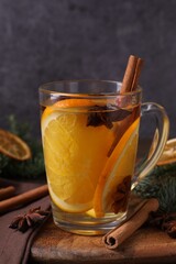 Tasty mulled wine with spices and orange slices in glass cup on table against gray background, closeup