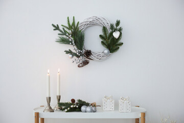 Christmas decor and burning candles on console table near white wall indoors. Interior design
