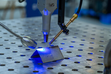 Close-up of high-precision automated laser welding or processing system at work on metal workpiece,...