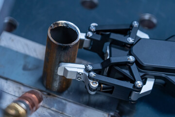 Advanced industrial robot arm gripper firmly securing rough, cut metal pipe on workbench, symbolizing manufacturing automation and precision engineering.