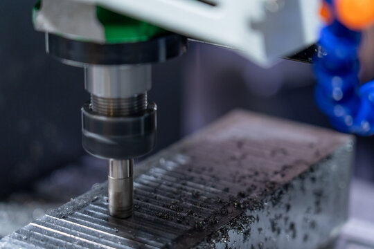 Close-up of high-precision CNC milling machine's rotating cutting tool actively machining metal workpiece, creating intricate grooves and producing metal chips during automated industrial manufacturin