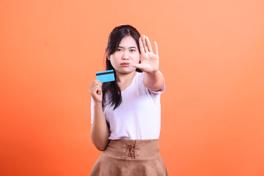 A woman refuses to use her credit card, making a stop hand gesture. This suggests financial prudence and control over expenses, isolated on orange background