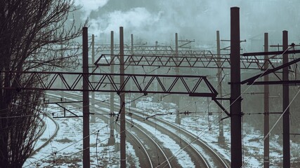 Winter railway tracks disappearing into fog under tangled wires
