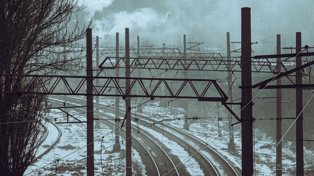 Winter railway tracks disappearing into fog under tangled wires