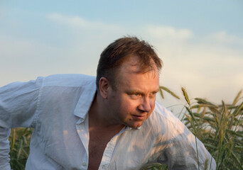 Man in white shirt leaning forward in rye field at sunset